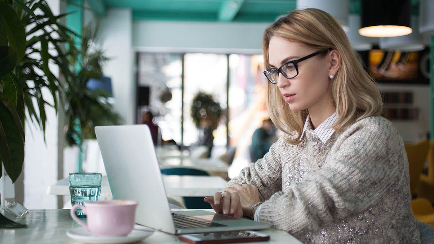 Concentrated female student preparing for exam in cafe. Busy young businesswoman using laptop to work. She reading business article. Lifestyle concept